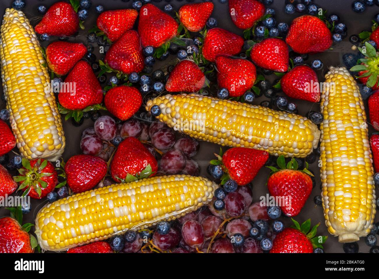Mais, Heidelbeeren, Erdbeeren und Trauben, die im Wasser im Waschbecken schwimmen Stockfoto
