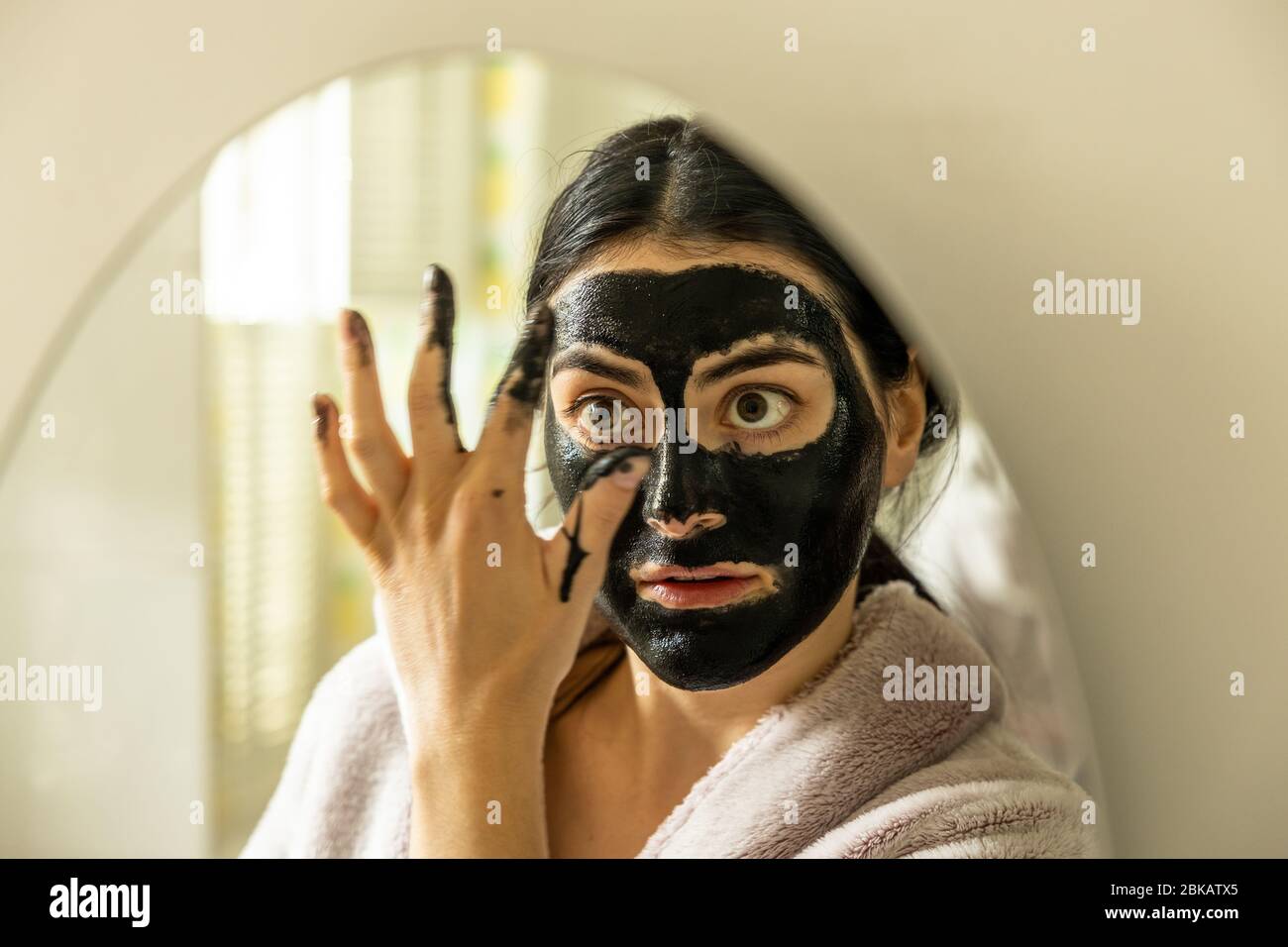 Eine junge Millennial Frau weiblich Anwendung einer Detox schwarze Kohle Peel off Gesichtsmaske Schönheitsbehandlung im Hause Bad London England UK Stockfoto
