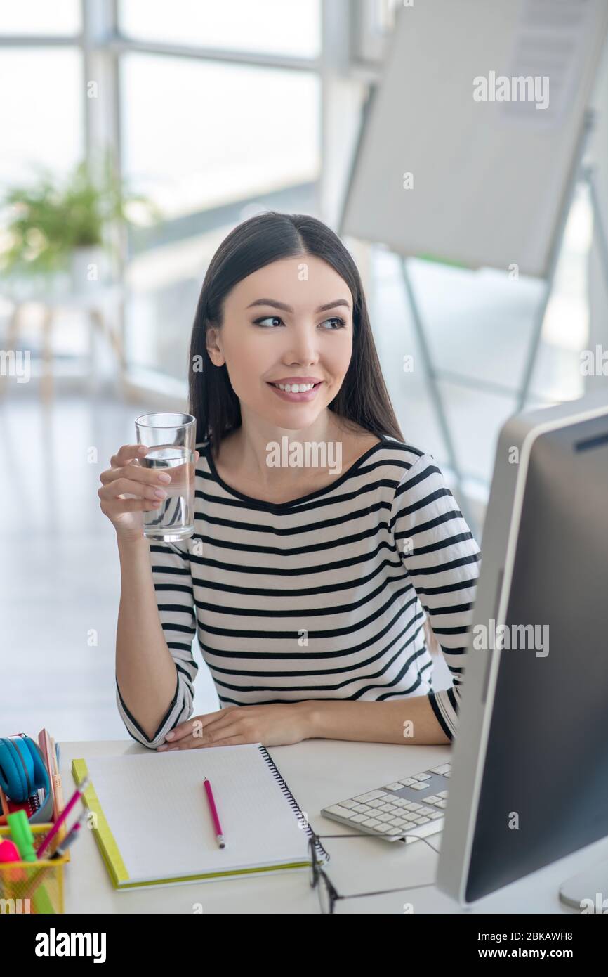 Ziemlich dunkelhaarige Frau mit einem Glas Wasser und lächelnd Stockfoto