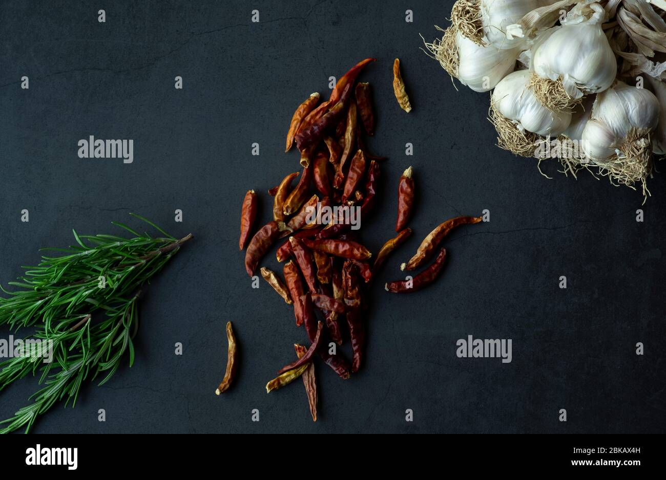 Rote Paprika, Knoblauch und frischer Rosmarin auf schwarzem Hintergrund. Blick von oben auf Bio-Lebensmittel aus dem Garten. Qualität und natürliche Lebensmittelmaterialien Stockfoto