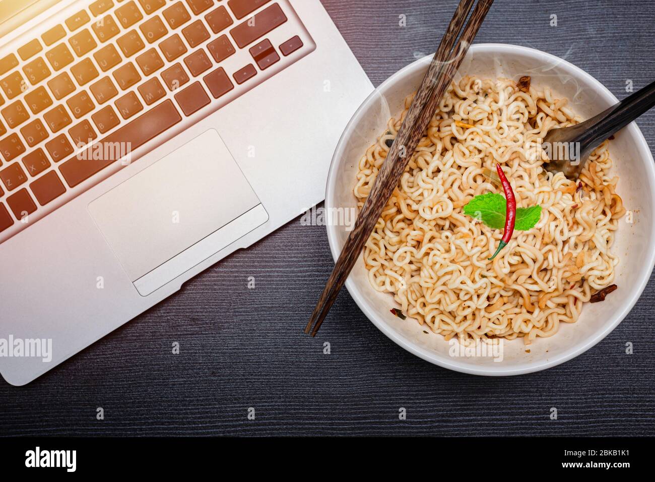 Instant-Nudeln mit Computer-Laptop für günstige und ungesunde Lebensmittel mit hohem Kohlenhydrat-Konzept essen. Stockfoto