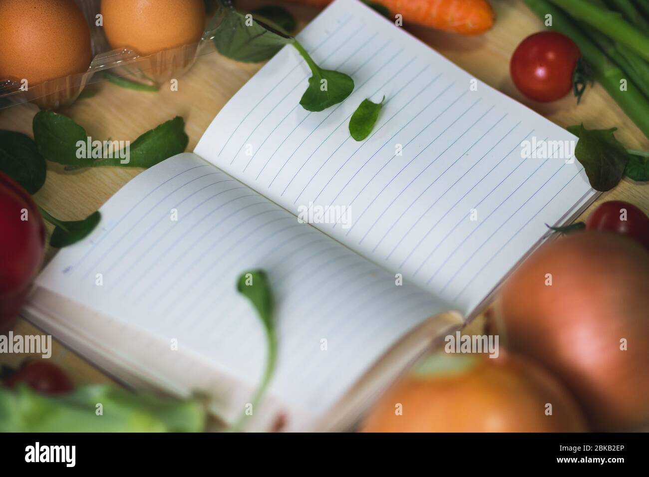 Offenes Notizbuch umgeben von Gemüse. Lebensmittelliste mit Gemüse um sie herum. Einkaufsliste mit Gemüse in der Umgebung. Einkaufen für Lebensmittel Stockfoto