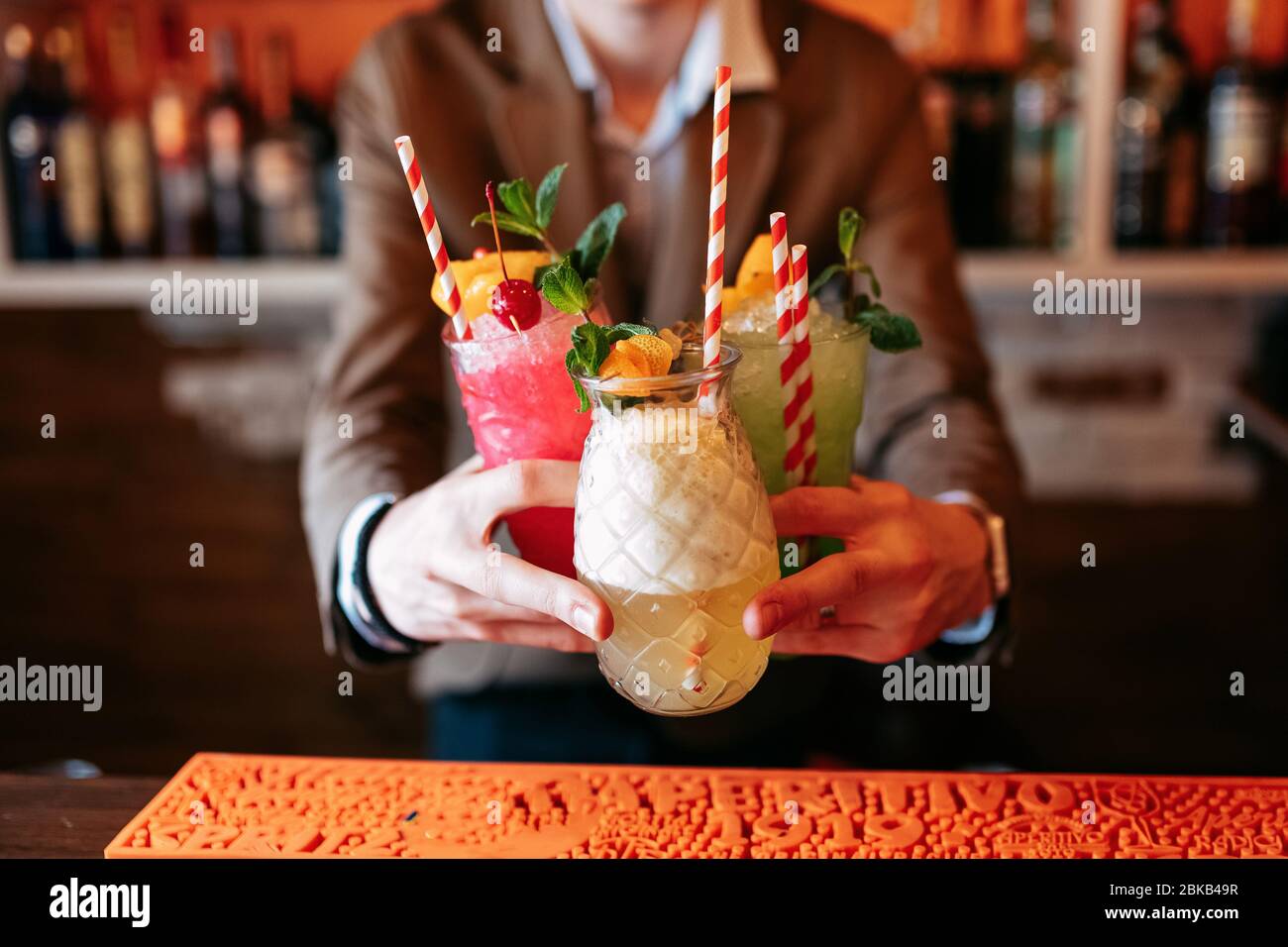 Der Barkeeper hält drei alkoholfreie Sommer-Cocktails. Alkoholisches Getränk auf der Basis von Tisch mit Eiswürfeln und Orangen. Stockfoto