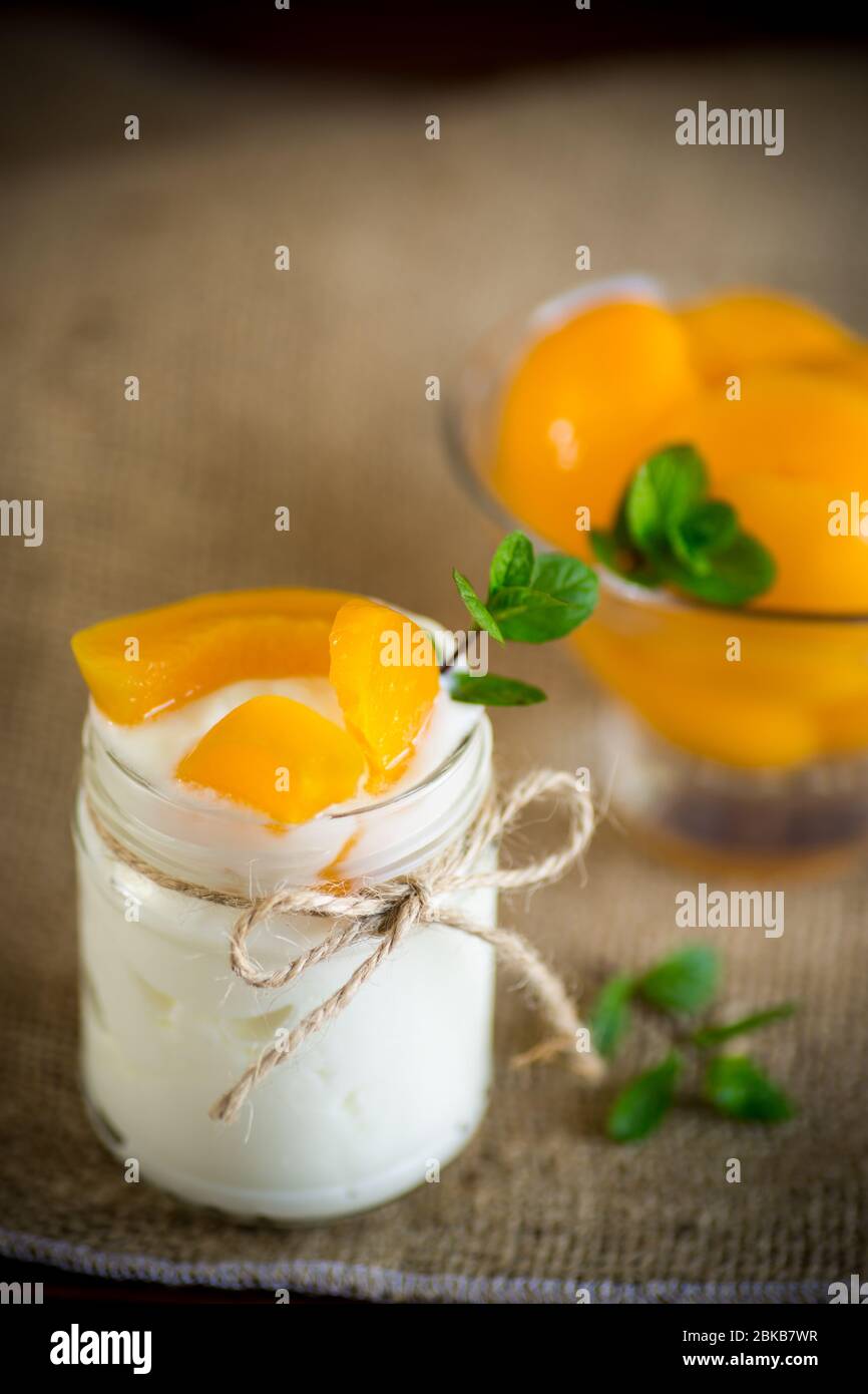 Hausgemachter süßer Joghurt mit Scheiben eingelegter Pfirsiche in einem Glasgefäß Stockfoto