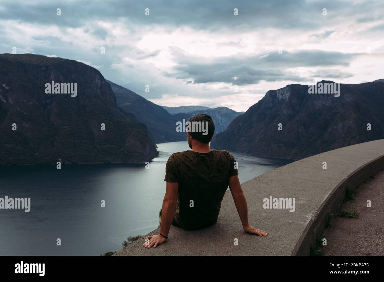 Ein Mann sitzt am Rande der Attika vor dem Hintergrund der Berge Norwegens und dem Himmel mit Wolken Stockfoto