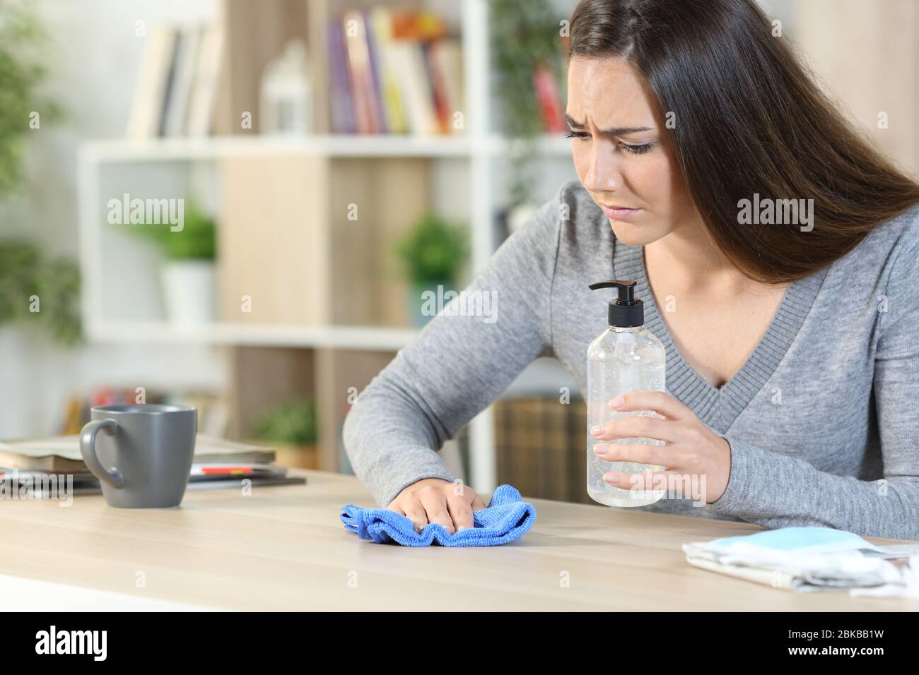 Besorgte Frau, die den Schreibtisch mit Desinfektionsmittel und Tuch reinigt und Ansteckungen vermeidet, die zu Hause auf einem Schreibtisch sitzen Stockfoto