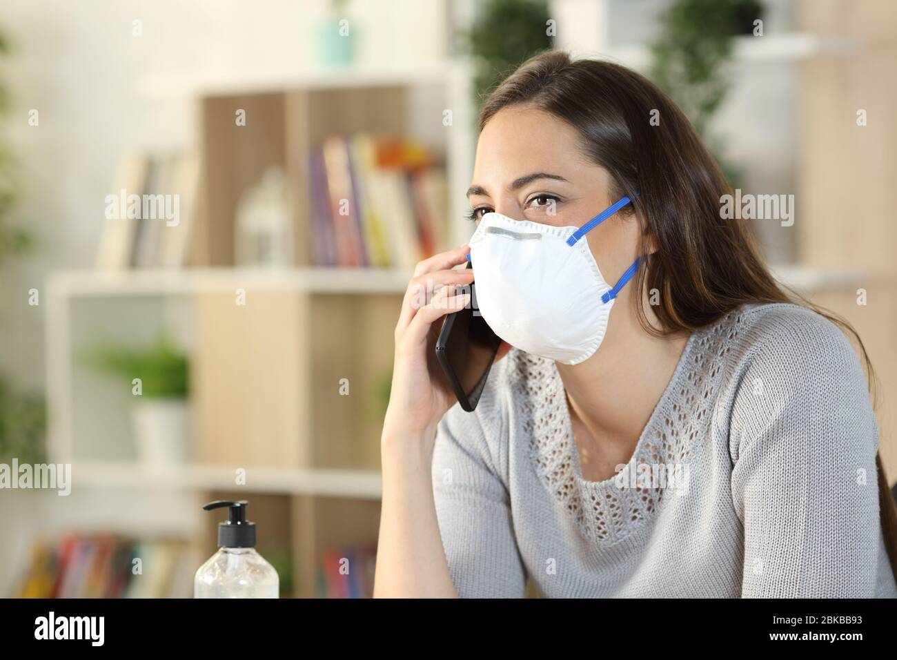 Glückliche Frau ruft am Smartphone in Coronavirus Confinement Maske zu Hause im Wohnzimmer tragen Stockfoto