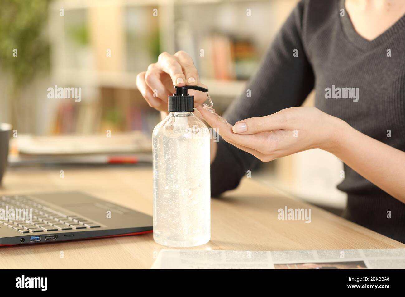 Nahaufnahme der Hände der Frau, die Desinfektionsmittel-Gel aus der Spenderflasche auf einem Schreibtisch zu Hause sitzt Stockfoto