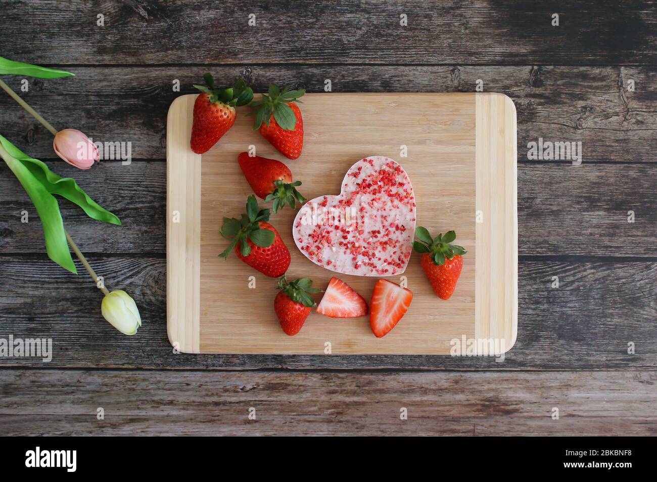 Erdbeerschokolade in Herzform auf einem Holzteller mit frischen Erdbeeren. Holztisch Hintergrund mit Tulpenblumen. Hintergrund der Grußkarte. Stockfoto