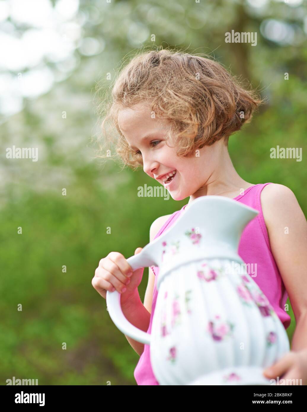Lächelndes Mädchen im Sommer trägt Wasser in Porzellan Krug Stockfoto
