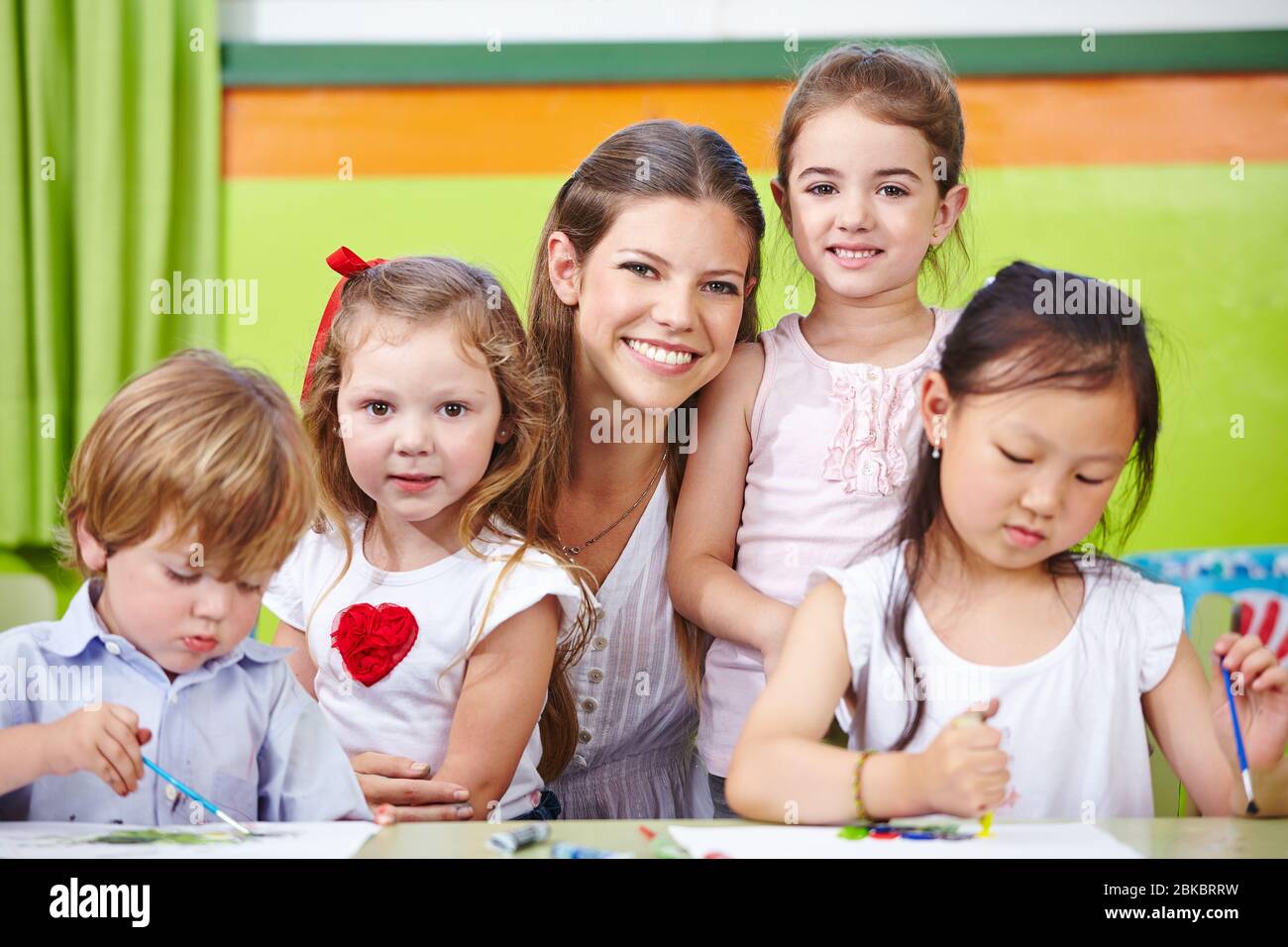 Lächelnde Erzieherin und glückliche Kinder malen im Kindergarten Stockfoto