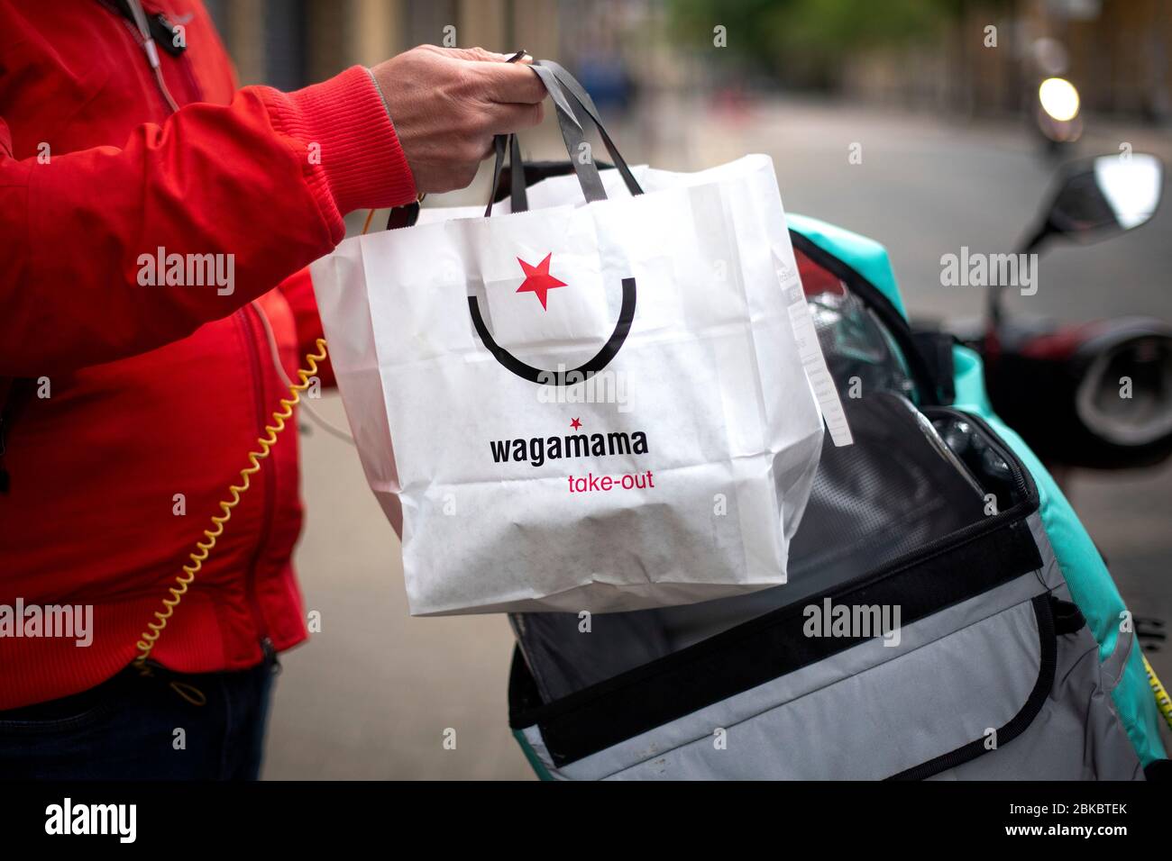 Ein Deliveroo-Fahrer holt eine Wagamama-Take-Away-Tasche von Wagamama Hackney Delivery Kitchen in East London ab, während Großbritannien weiterhin in der Sperre bleibt, um die Ausbreitung des Coronavirus einzudämmen. Stockfoto