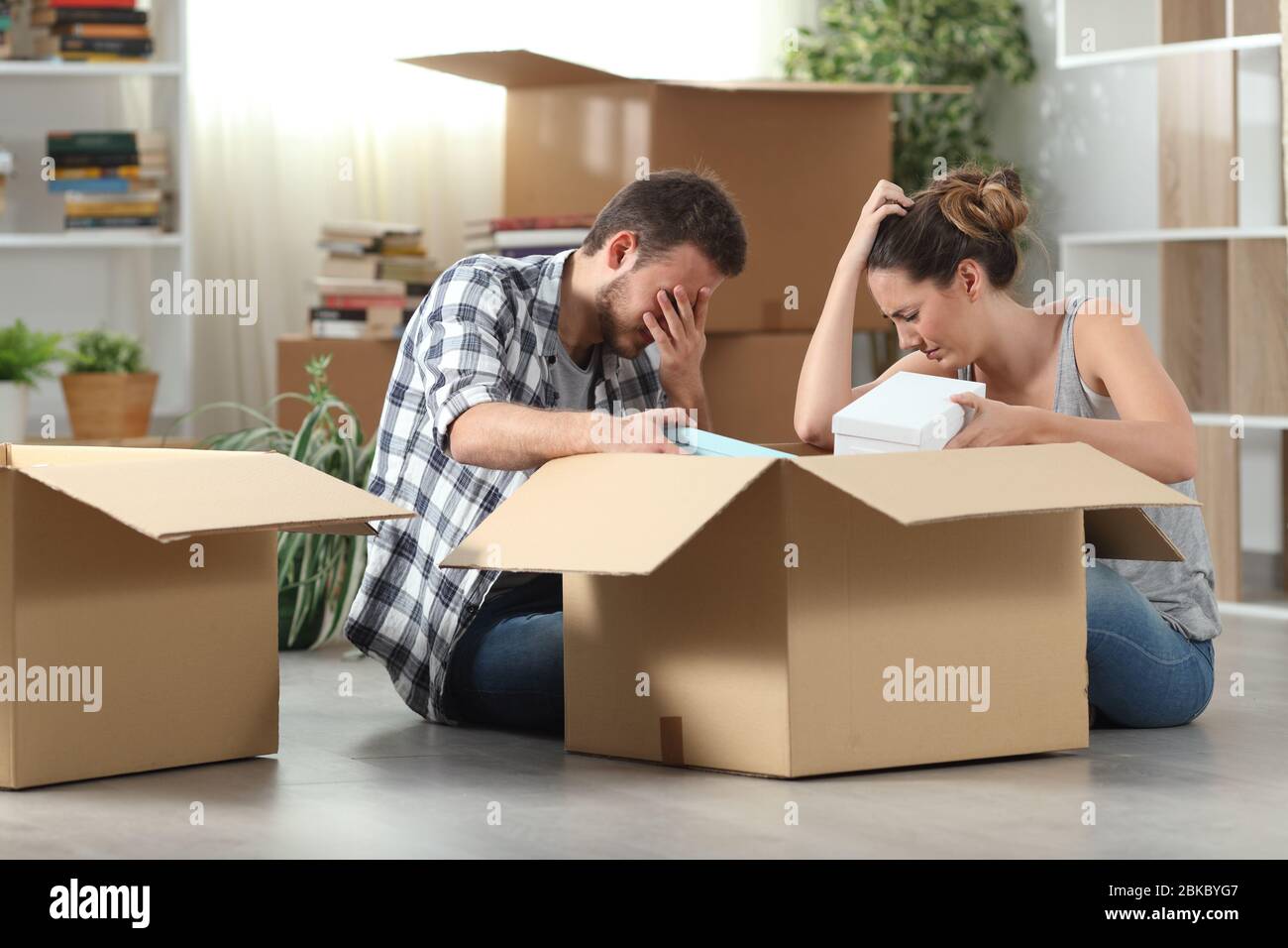 Zwei traurige, vertreibte Mieter, die nach Hause umziehen und auf dem Boden sitzende Gegenstände packen Stockfoto