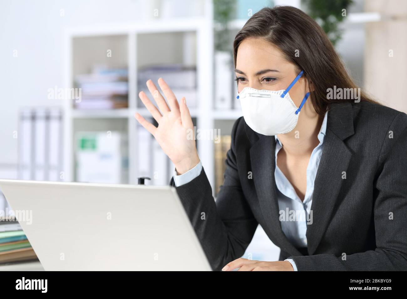 Glückliche Exekutive Frau schaut Laptop Webcam auf Videocall Gruß Vermeidung covid-19 mit Maske im Büro sitzen Stockfoto