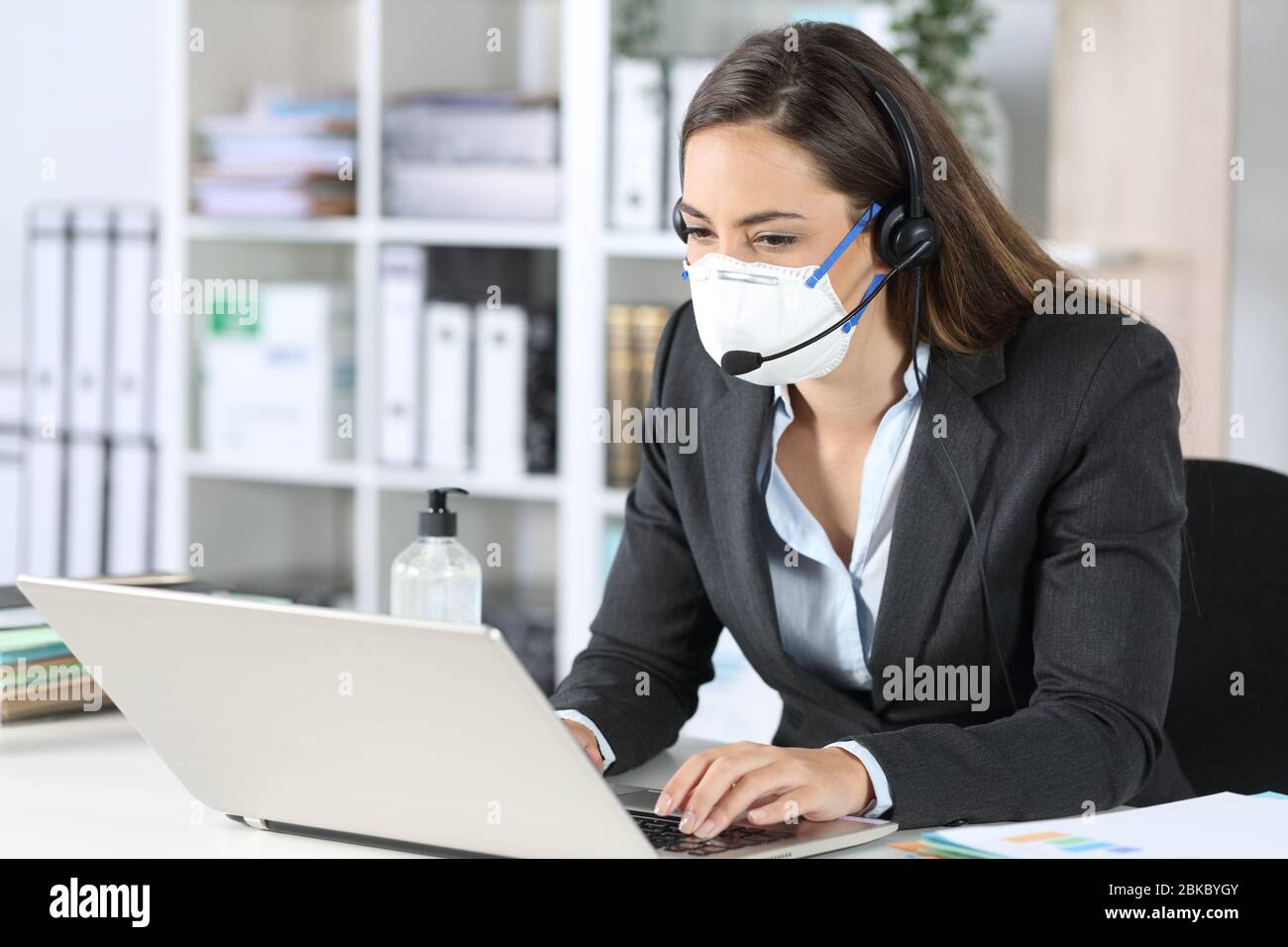 Telemarketerin Frau arbeitet auf Laptop Vermeidung covid-19 mit Maske sitzt auf einem Schreibtisch im Büro Stockfoto