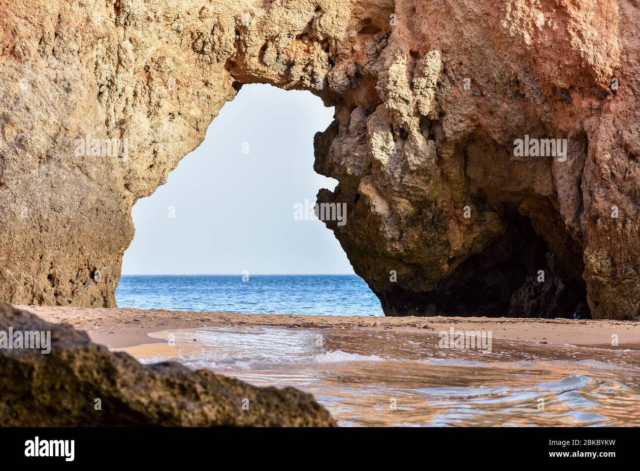 Leerer Strand zwischen Klippen und natürlichen Torbogen, durch den man das Meer sehen kann. Unbevölkerten Reisekonzept. Algarve, Portugal. Algarve, Portugal Stockfoto