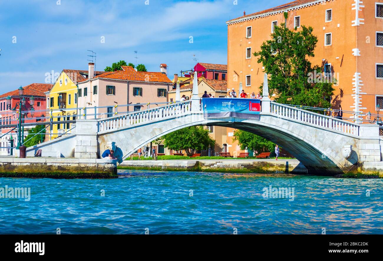 Historische Gebäude entlang der Uferpromenade und der Fußgängerbrücke von Puente Arsenale über den Kanal Rio dell Arsenale, von einem Boot aus gesehen Lagune von Venedig blaues Wasser Stockfoto