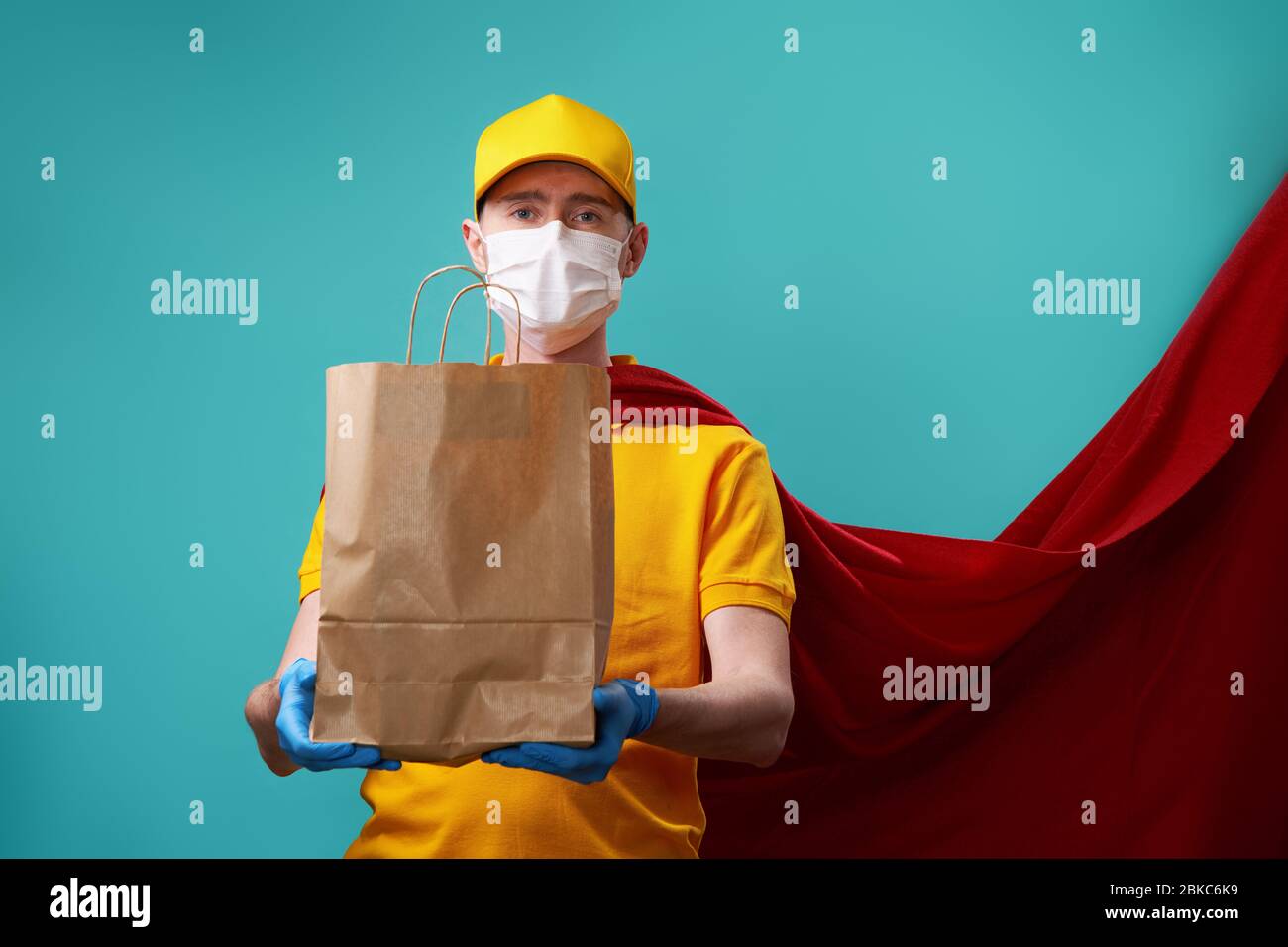 Kurier mit Tasche trägt medizinische Gesichtsmaske in Superhelden Mantel. Konzept der Superheldentum Kurier während Coronavirus Ausbruch. Stockfoto