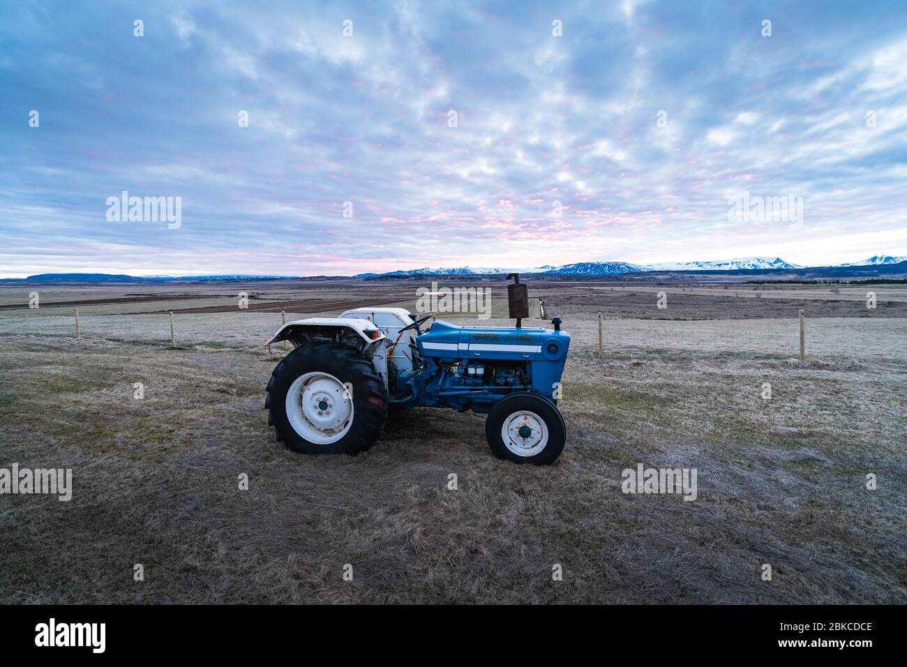 Bild der Landwirtschaft. Ein kleiner Traktor auf einem Feld während der Sonnenuntergangszeit. Landwirtschaft in Island, Skandinavien. Hintergrundfoto eines Traktors Stockfoto