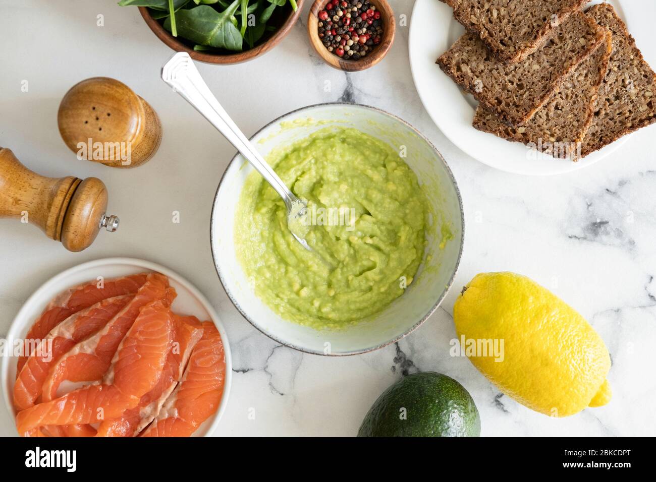 Avocado-Sauce in Schüssel und Zutaten für ein gesundes leckeres Sandwich mit Roggenbrot, geräuchertem Lachs Fisch, Avocado-Püree und Baby-Spinat-Blatt Stockfoto