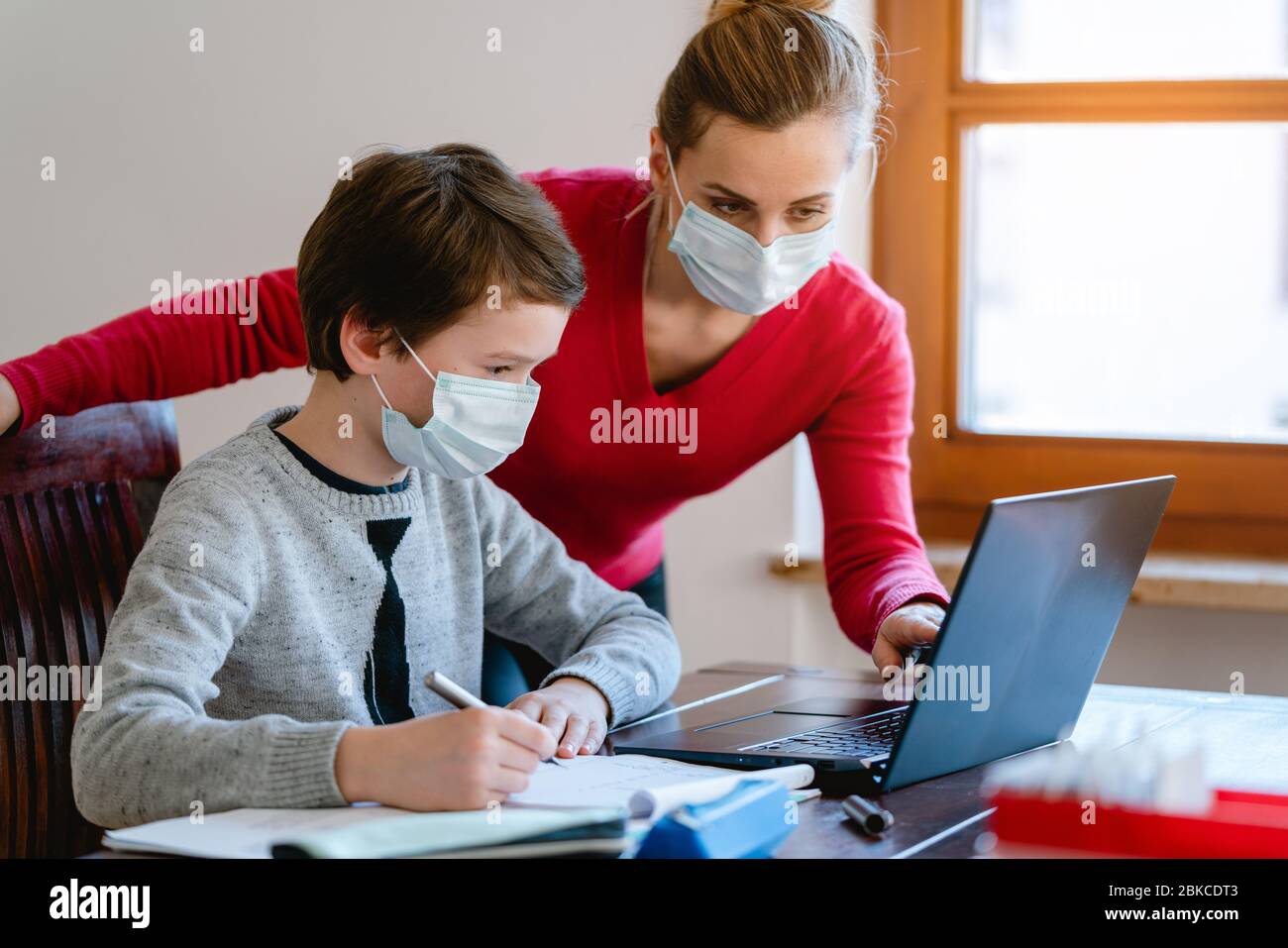 Mutter und Sohn im Video-Chat mit Lehrer, die Masken tragen Stockfoto