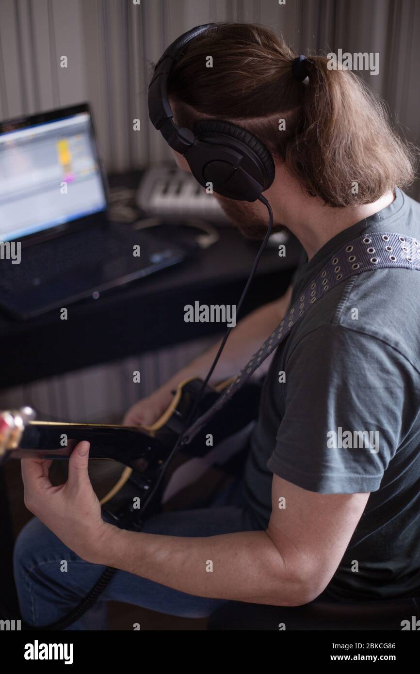Bärtiger Mann Musiker Musik spielen und komponieren ein Lied mit E-Gitarre Klavier und Laptop-Computer, während im Wohnzimmer sitzen, Corona Virus quar Stockfoto