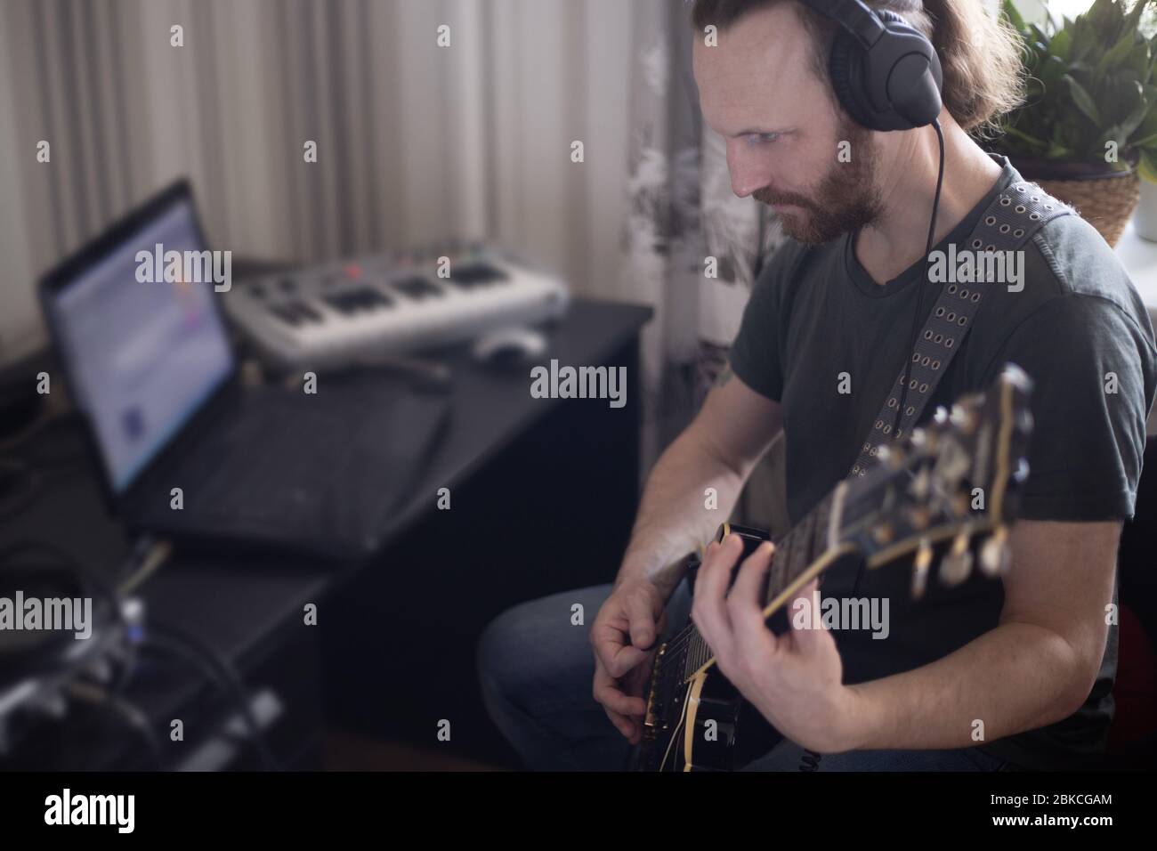 Bärtiger Mann Musiker Musik spielen und komponieren ein Lied mit E-Gitarre Klavier und Laptop-Computer, während im Wohnzimmer sitzen, Corona Virus quar Stockfoto