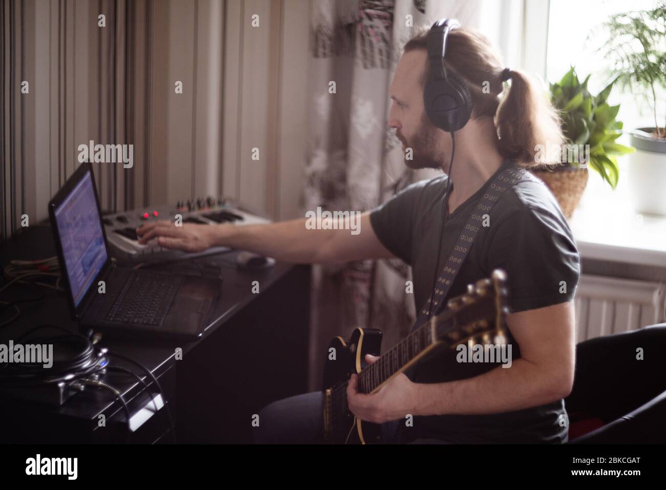 Bärtiger Mann Musiker Musik spielen und komponieren ein Lied mit E-Gitarre Klavier und Laptop-Computer, während im Wohnzimmer sitzen, Corona Virus quar Stockfoto