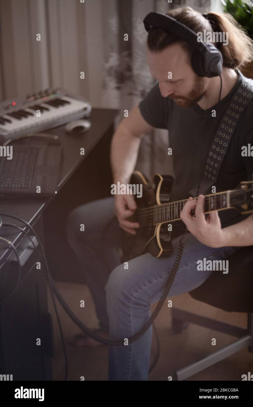 Bärtiger Mann Musiker Musik spielen und komponieren ein Lied mit E-Gitarre Klavier und Laptop-Computer, während im Wohnzimmer sitzen, Corona Virus quar Stockfoto