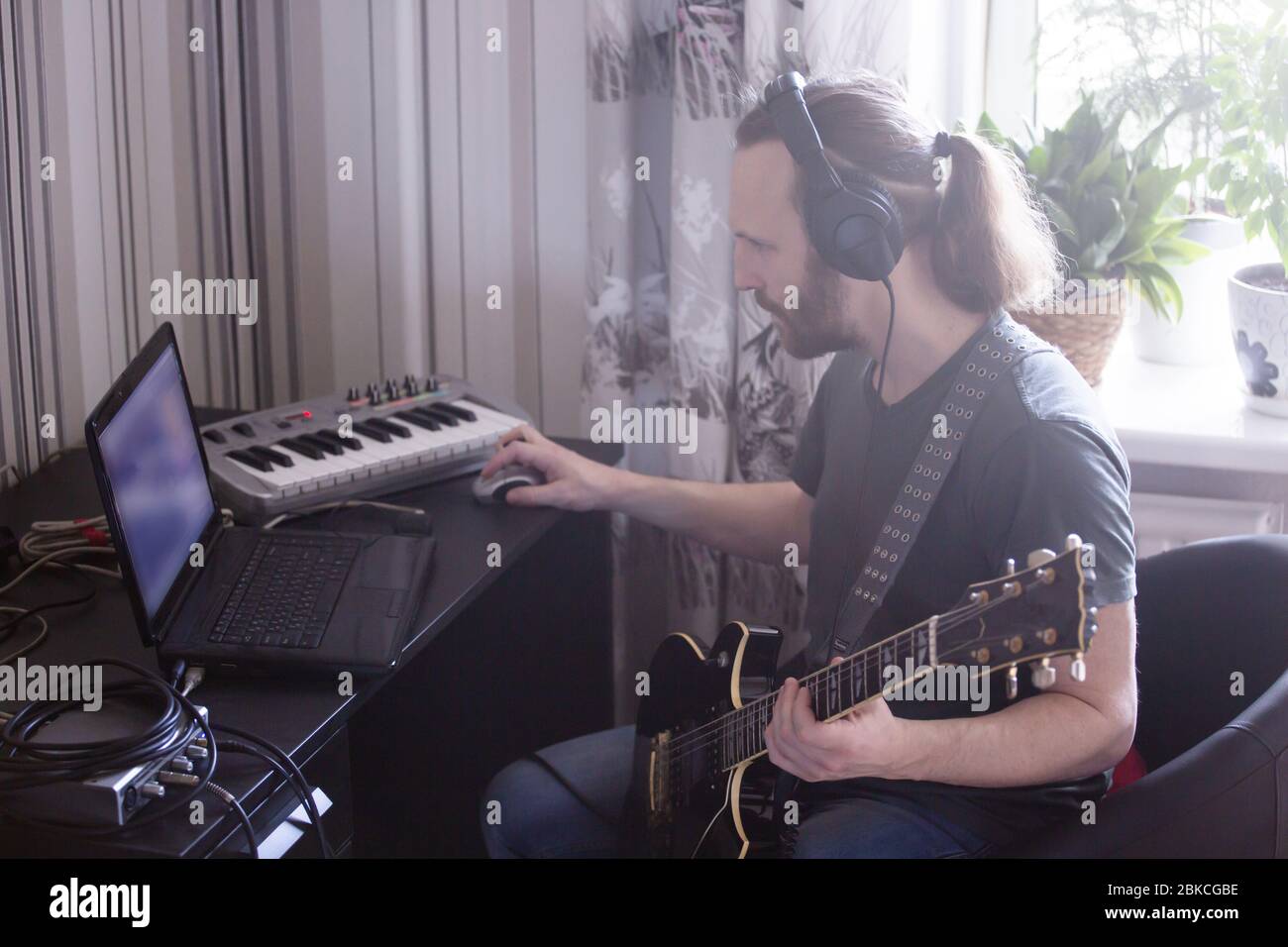 Bärtiger Mann Musiker Musik spielen und komponieren ein Lied mit E-Gitarre Klavier und Laptop-Computer, während im Wohnzimmer sitzen, Corona Virus quar Stockfoto