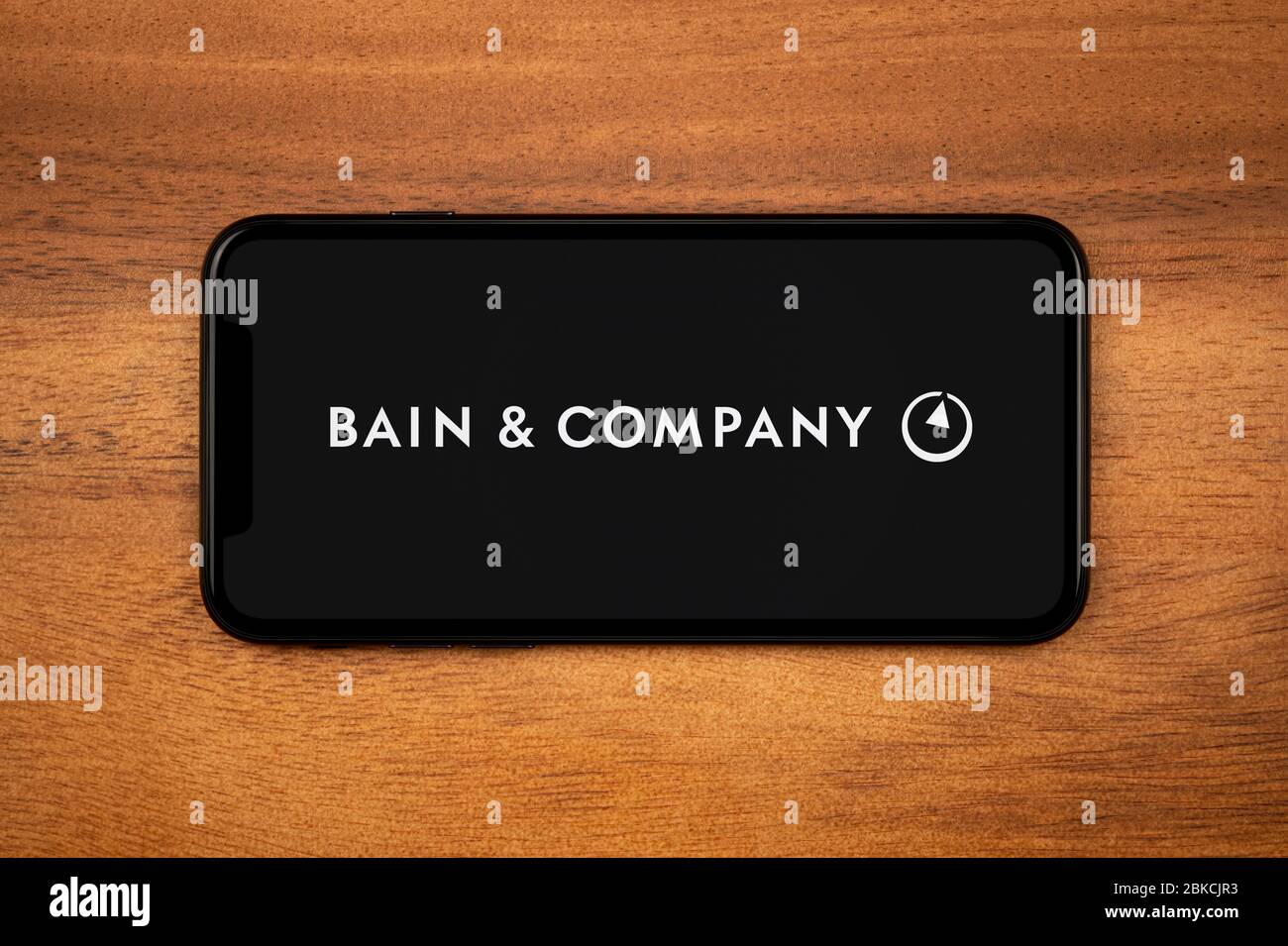Ein Smartphone mit dem Bains & Company Logo liegt auf einem einfachen Holztisch (nur zur redaktionellen Verwendung). Stockfoto