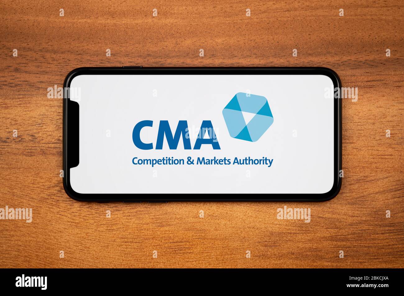 Ein Smartphone mit dem CMA-Logo (Competition and Markets Authority) liegt auf einem einfachen Holztisch (nur redaktionelle Verwendung). Stockfoto