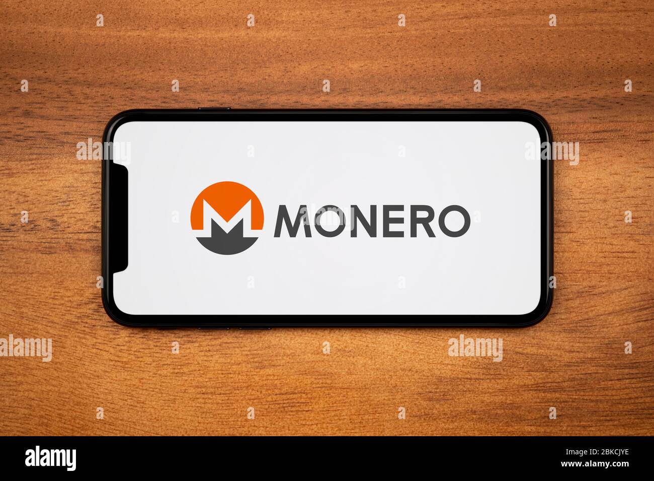 Ein Smartphone mit dem Monero Logo liegt auf einem einfachen Holztisch (nur für redaktionelle Verwendung). Stockfoto