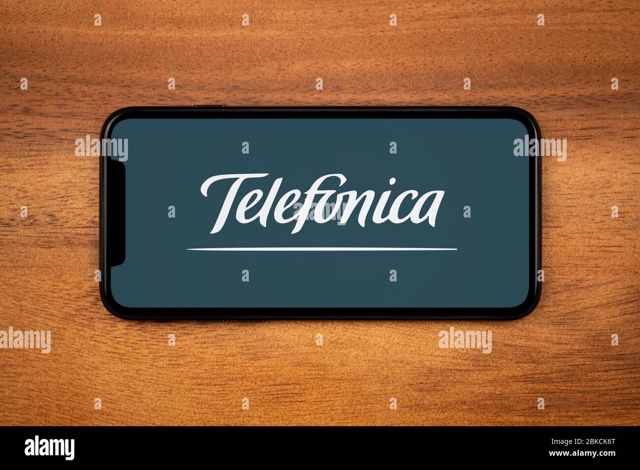 Ein Smartphone mit dem Telefonica-Logo liegt auf einem einfachen Holztisch (nur redaktionelle Verwendung). Stockfoto