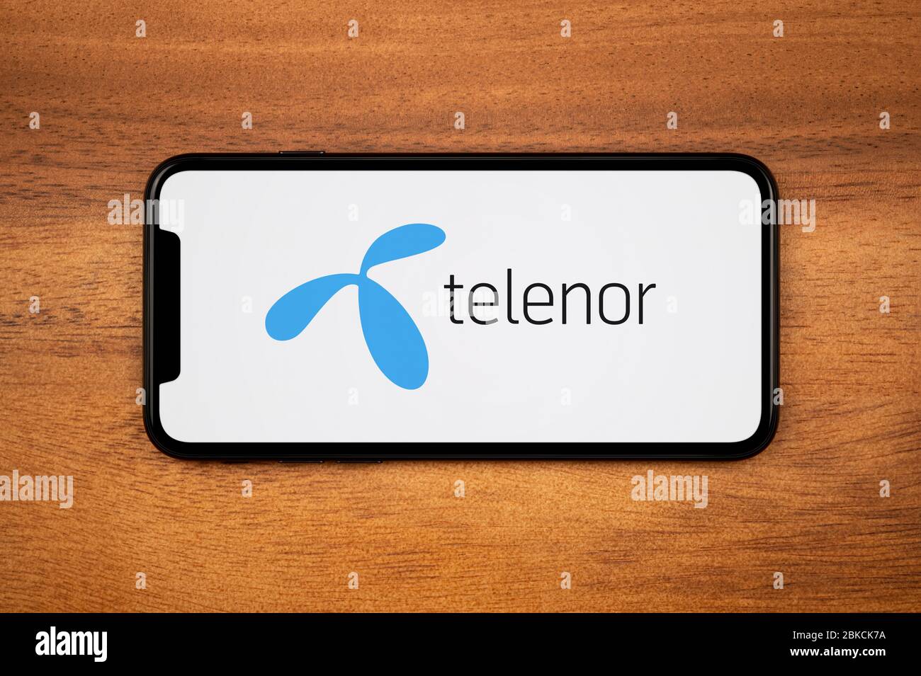Ein Smartphone mit dem Telenor-Logo liegt auf einem einfachen Holztisch (nur für redaktionelle Verwendung). Stockfoto