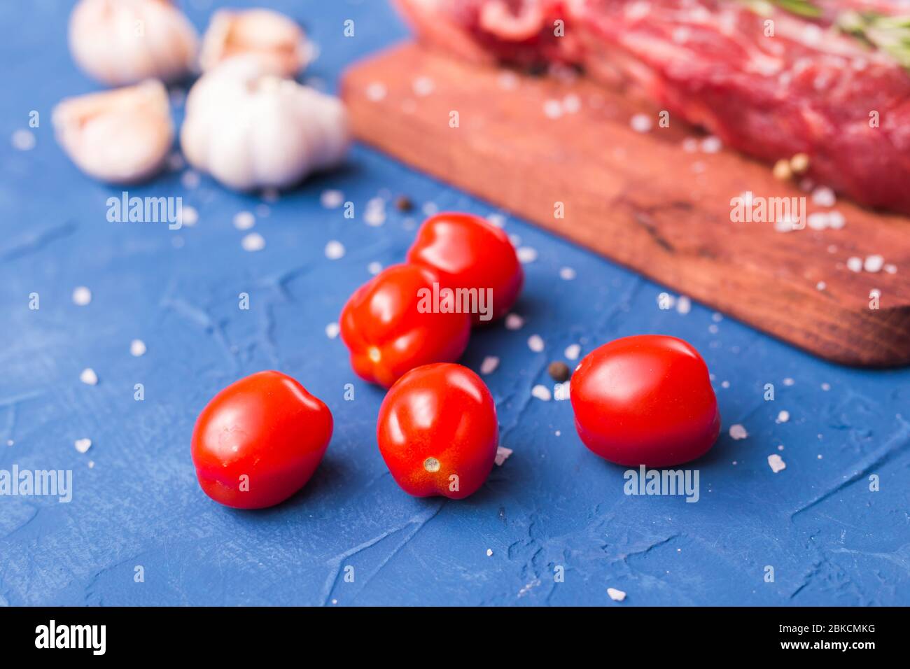 Nahaufnahme von frischen kleinen Tomaten auf blauem Hintergrund. Zutaten zum Kochen von Fleisch. Stockfoto