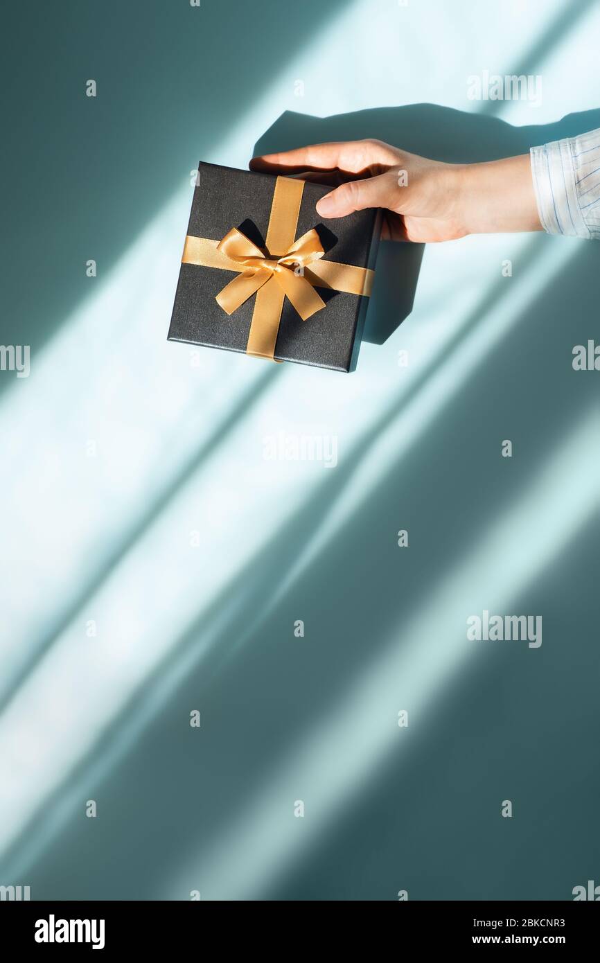 Vertikales Foto mit Geschenkbox in einer weiblichen Hand auf Sonnenlichter auf blauem Hintergrund. Flaches Layout, Draufsicht, Platz für Text. Stockfoto