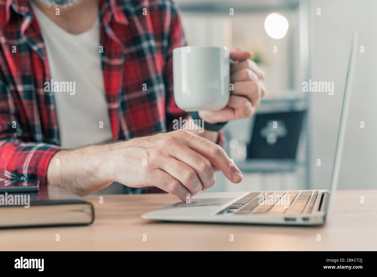 Freiberuflicher Mitarbeiter, der Laptop-Computer verwendet und Kaffee im Home Office trinkt, selektiver Fokus auf Hände Stockfoto