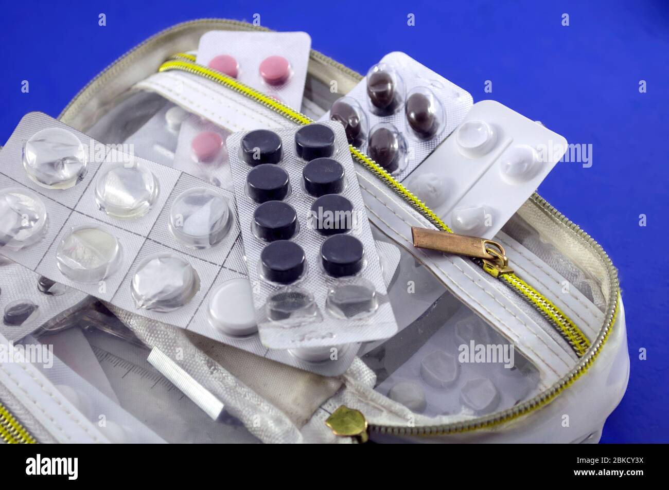Weiße offene Handtasche mit halbleeren Blisterpackungen aus rosa, weißen und braunen Tabletten auf blauem Hintergrund, Stockfoto