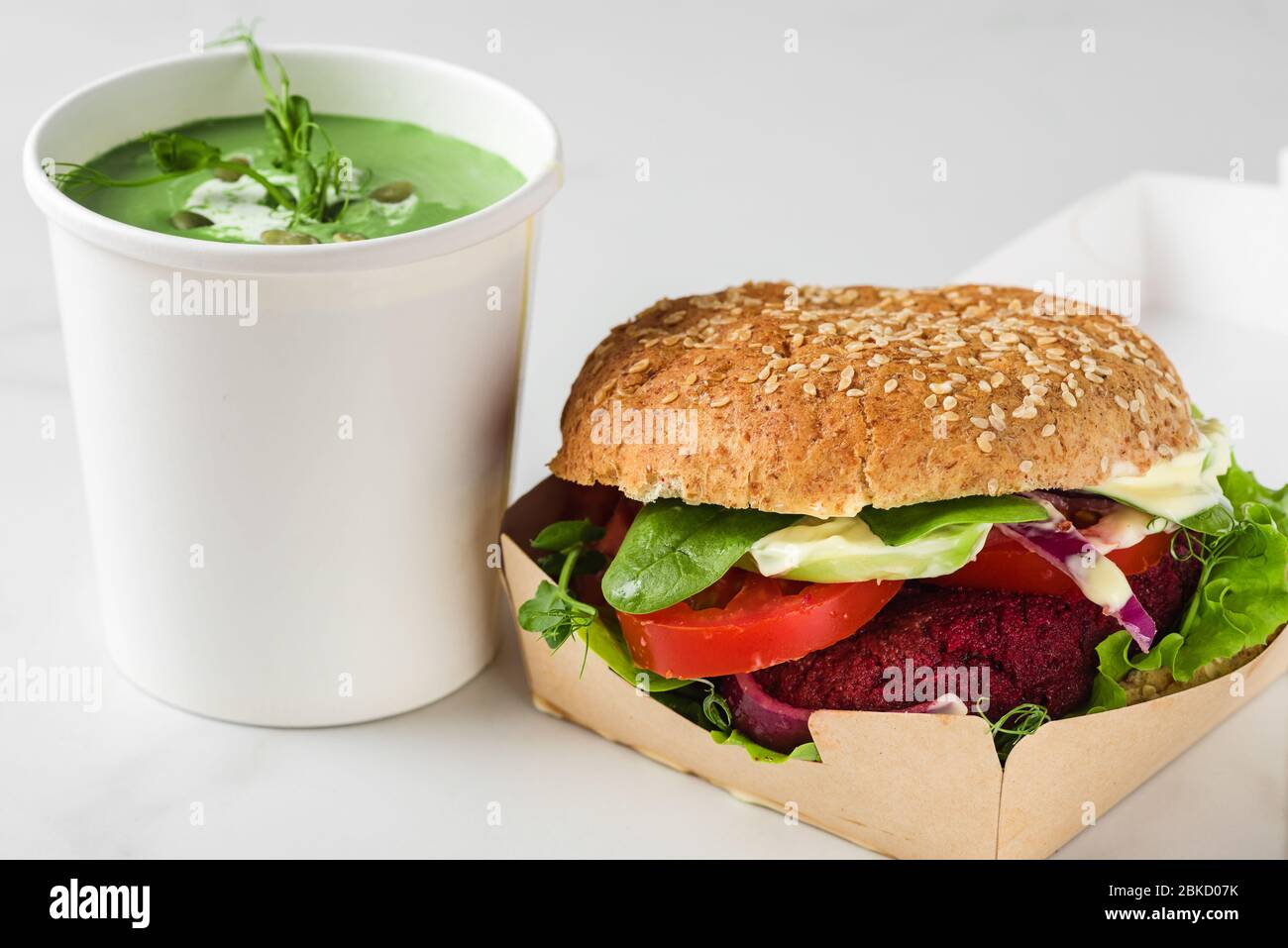 Lieferung von veganen Lebensmitteln. Veganer Rote Bete Burger mit Avocado in Öko-Papierbox mit Erbsensuppe in Einwegbecher. Gesunde Ernährung Mittagessen zum Mitnehmen Stockfoto