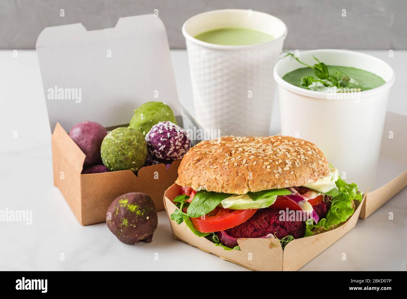 Lieferung von Lebensmitteln. Vegane Rübenburger und Energiebällchen in Öko-Pappkartons mit Erbsensuppe und Matcha Latte in Einwegbechern. Gesunde Ernährung Mittagessen zu ta Stockfoto