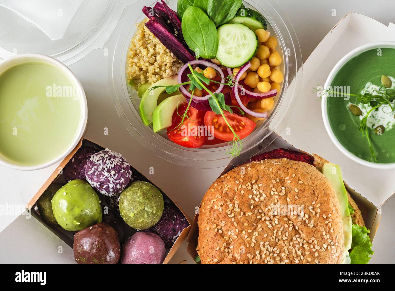 Gesunde vegane Lebensmittel liefern. Verpackter Burger, buddha-Schüssel Salat, grüne Suppe, Energiebällchen und Matcha Latte in Kisten und Tassen. Draufsicht. Flach gelegt. Eco-D Stockfoto