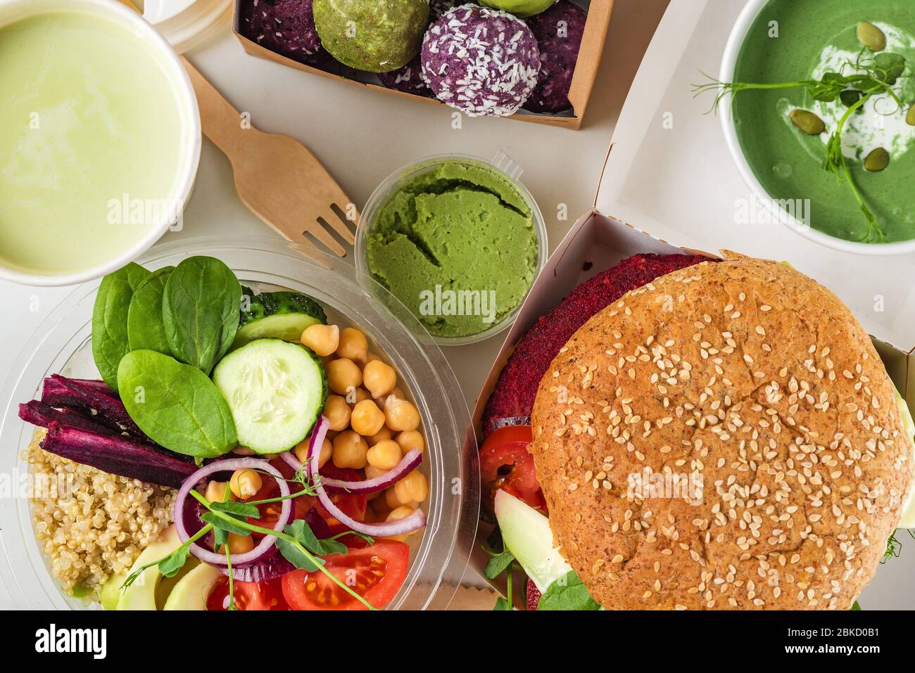 Gesunde vegane Lebensmittel liefern. Buddha Schüssel Salat, Burger, Suppe, Dessert und Matcha Latte in Kisten und Tassen verpackt. Draufsicht. Flaches Lay. Restaurant-Menü en Stockfoto