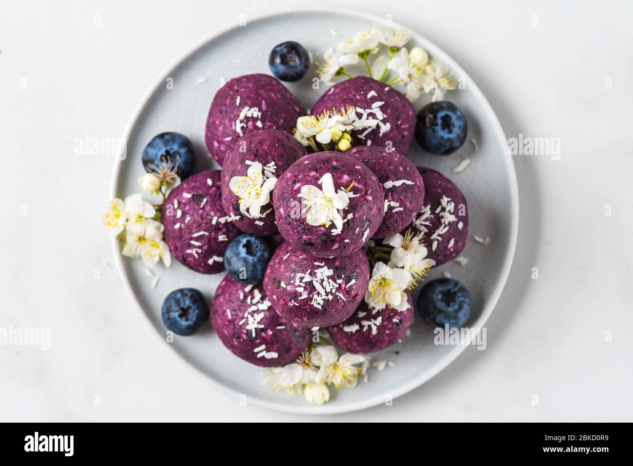 Keine backen Heidelbeere und acai Energie Bissen oder Kugeln aus Nüssen, Kokosflocken und Datteln mit Blumen serviert. Draufsicht. Gesunde vegane Lebensmittel Dessert Stockfoto