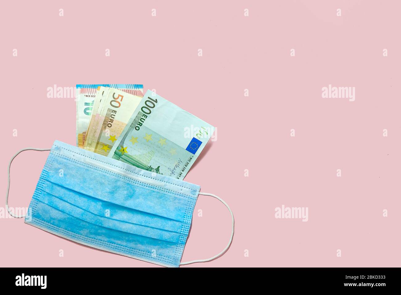 Quarantäne Geschäft.Euro-Banknoten und medizinische Maske auf einem rosa Hintergrund. Konzept der Finanzkrise während der Coronavirus-Pandemie. Stockfoto