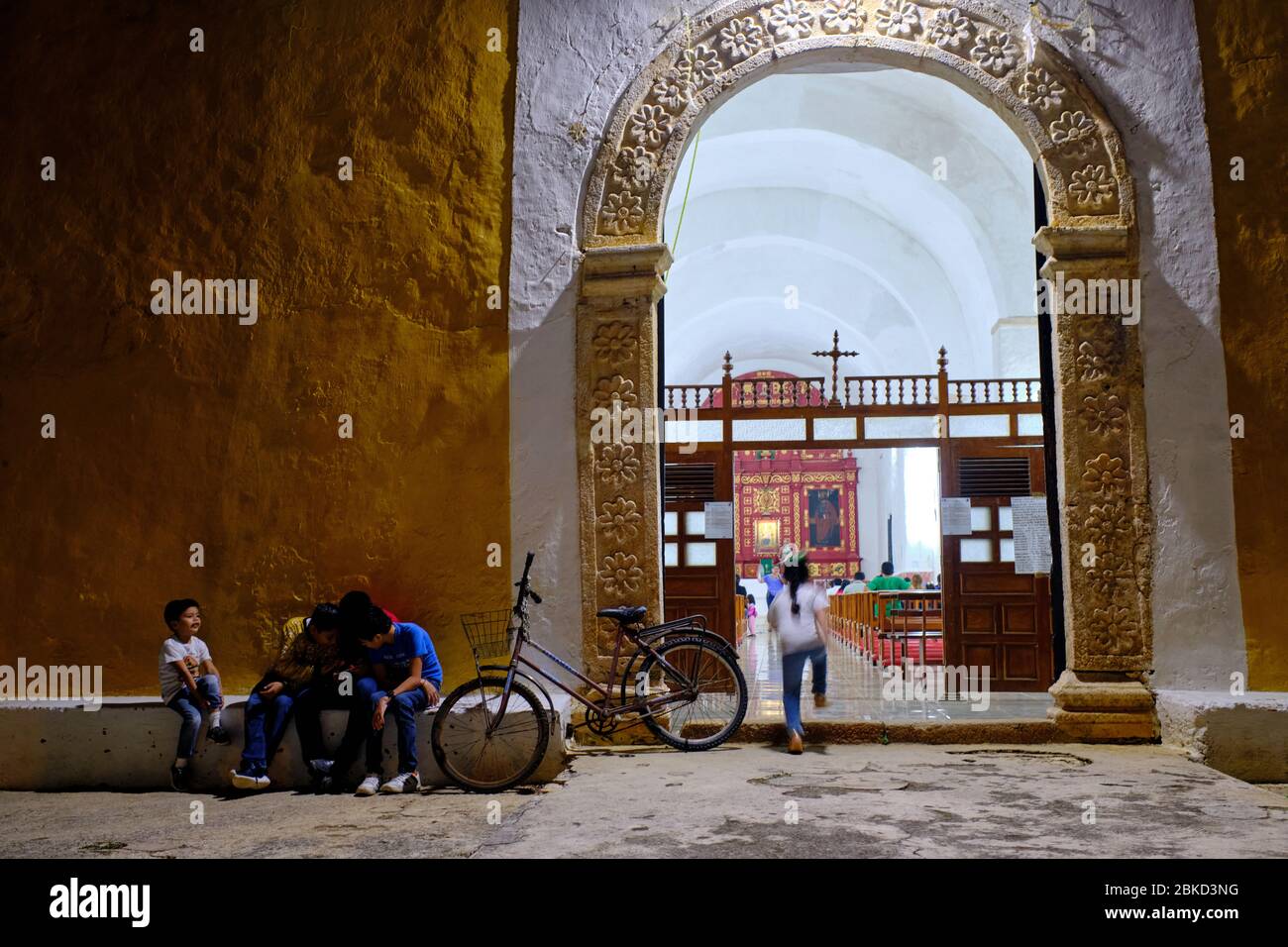 Kinder spielen mit dem Smartphone an der Tür einer Kolonialkirche in Valladolid, während im Inneren eine Messe gefeiert wird. Stockfoto