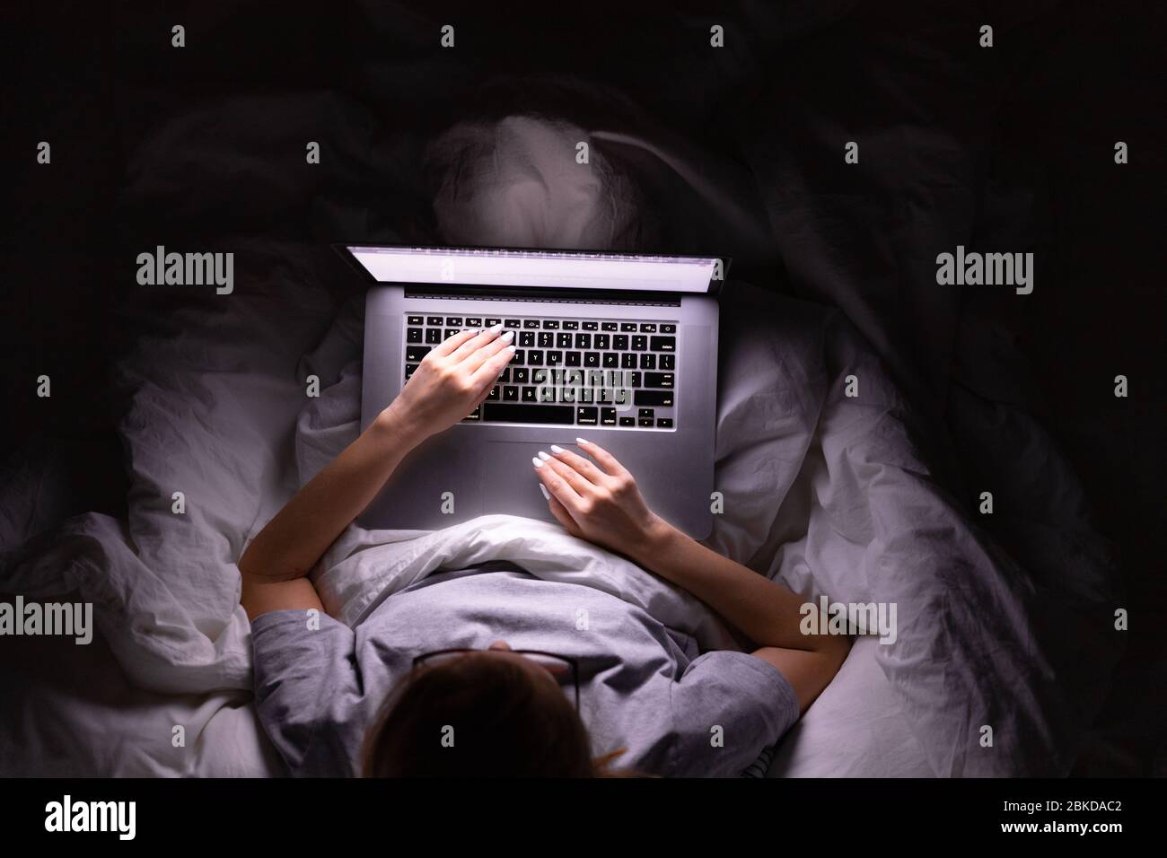 Frau in Brille im Bett liegend mit Decke bedeckt und arbeiten auf Laptop spät in der Nacht, kann nicht schlafen, Nachrichten-Suche über Covid-19 oder teilen sozialen medi Stockfoto