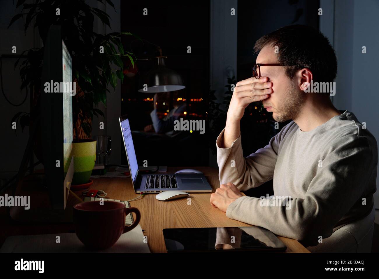 Müde Freelancer Mann reibt sich die Augen, sitzt am Desktop-PC / Laptop spät in der Nacht, während der Zeit der Selbstisolierung und Remote-Arbeit zu Hause, fällt Stockfoto