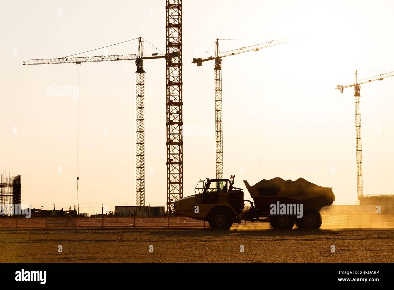 Gruppe Turmkrane und Silhouette von Kipper auf der Baustelle, Sonnenuntergang Himmel Hintergrund. Zukünftiger Wohnhochhauskomplex Stockfoto