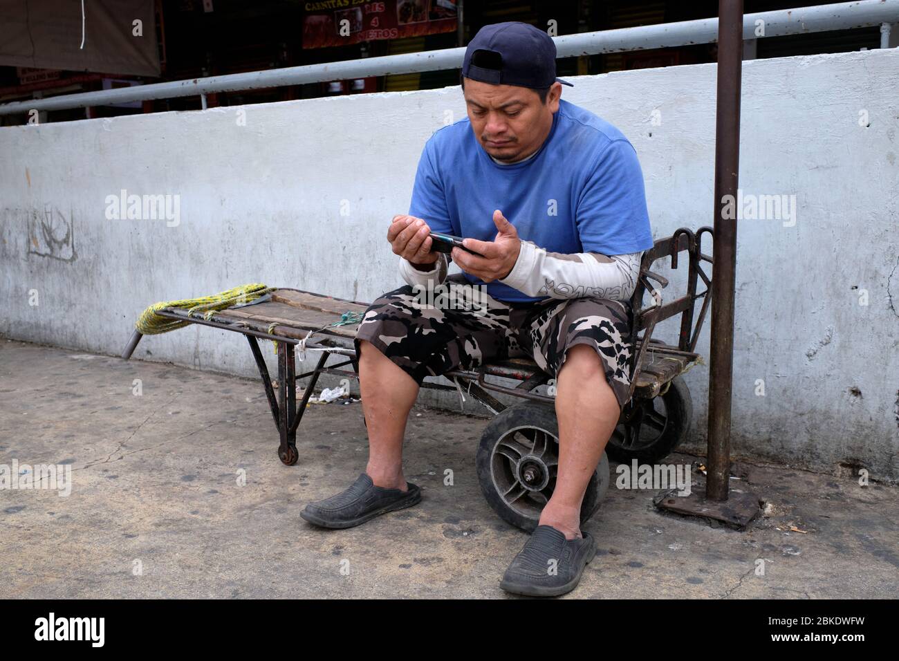 Der Portier ruht sich aus und überprüft sein Handy, sitzt in einer Schubkarre auf dem städtischen Markt von Merida. Stockfoto